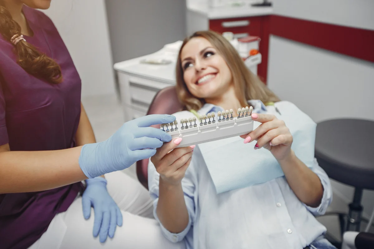 Dentist showing porcelain veneers shade options to smiling patient in clinic — customizing perfect natural-looking smile with CMC’s cosmetic dentistry.